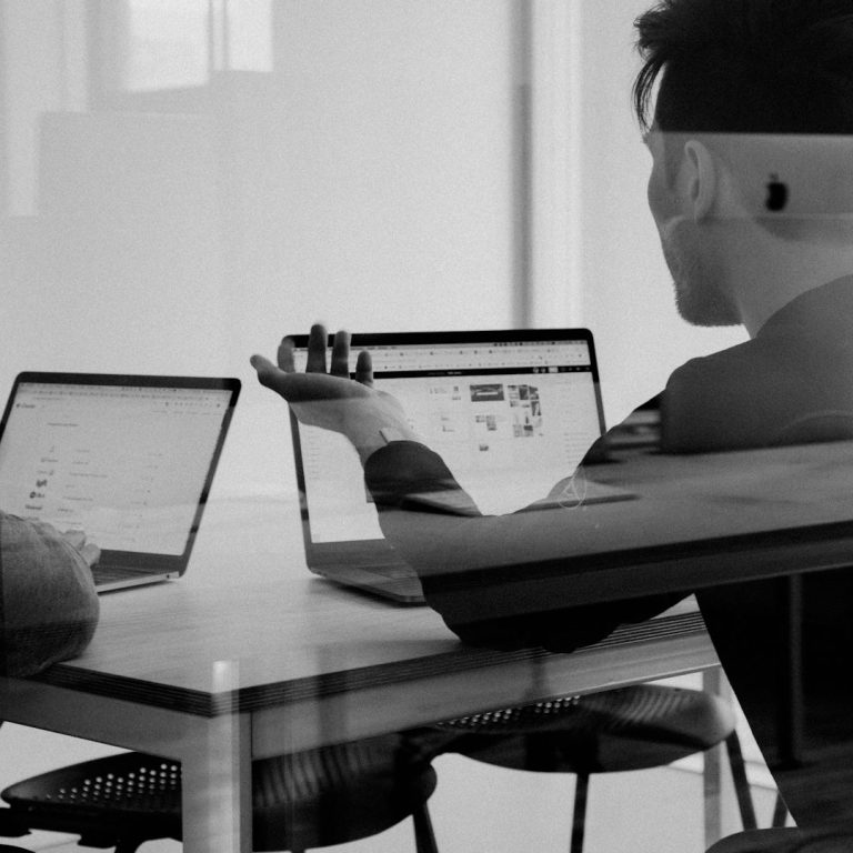 Projektmanagement und Implementierung Zwei Personen sitzen an Tischen und arbeiten an Laptops in einem modernen Büro.