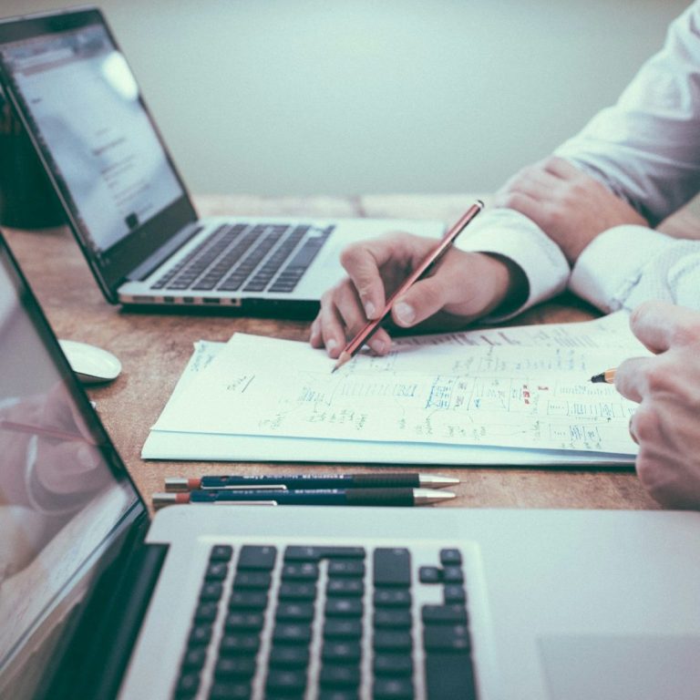 Digitale Strategie und Transformation Zwei Personen arbeiten an Laptops und notieren Ideen auf einem Blatt Papier.